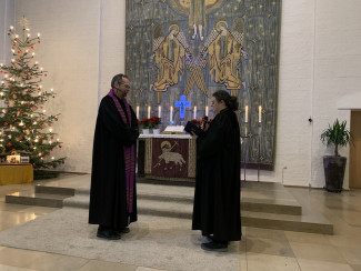 Pfarrer Bernd Reuther (links) wird von Dekanin Karolin Gerleigner in seinen Dienst eingeführt. Sie stehen vor einem Altar und tragen beiden Talar.